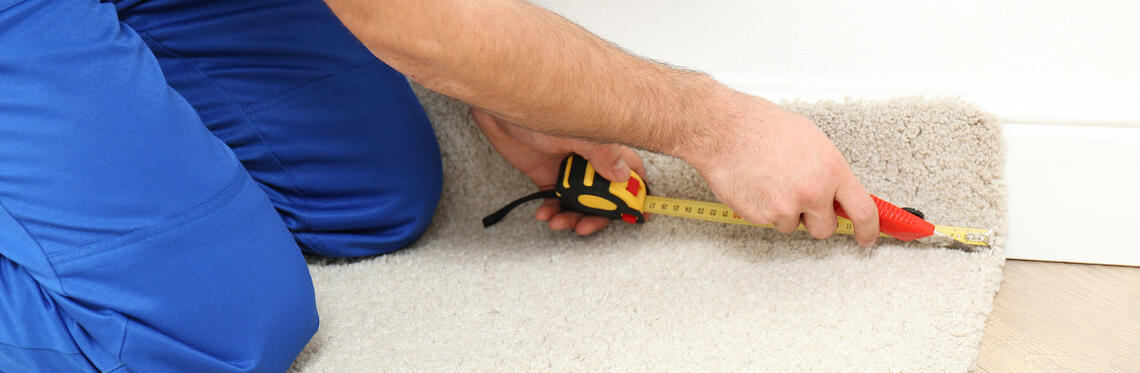 A carpet repairer measuring the carpet along a skirting board