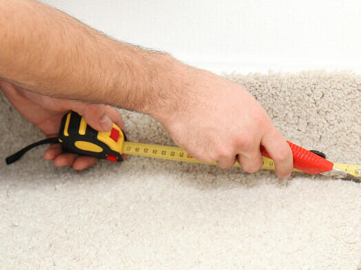 A carpet repairer measuring the carpet along a skirting board